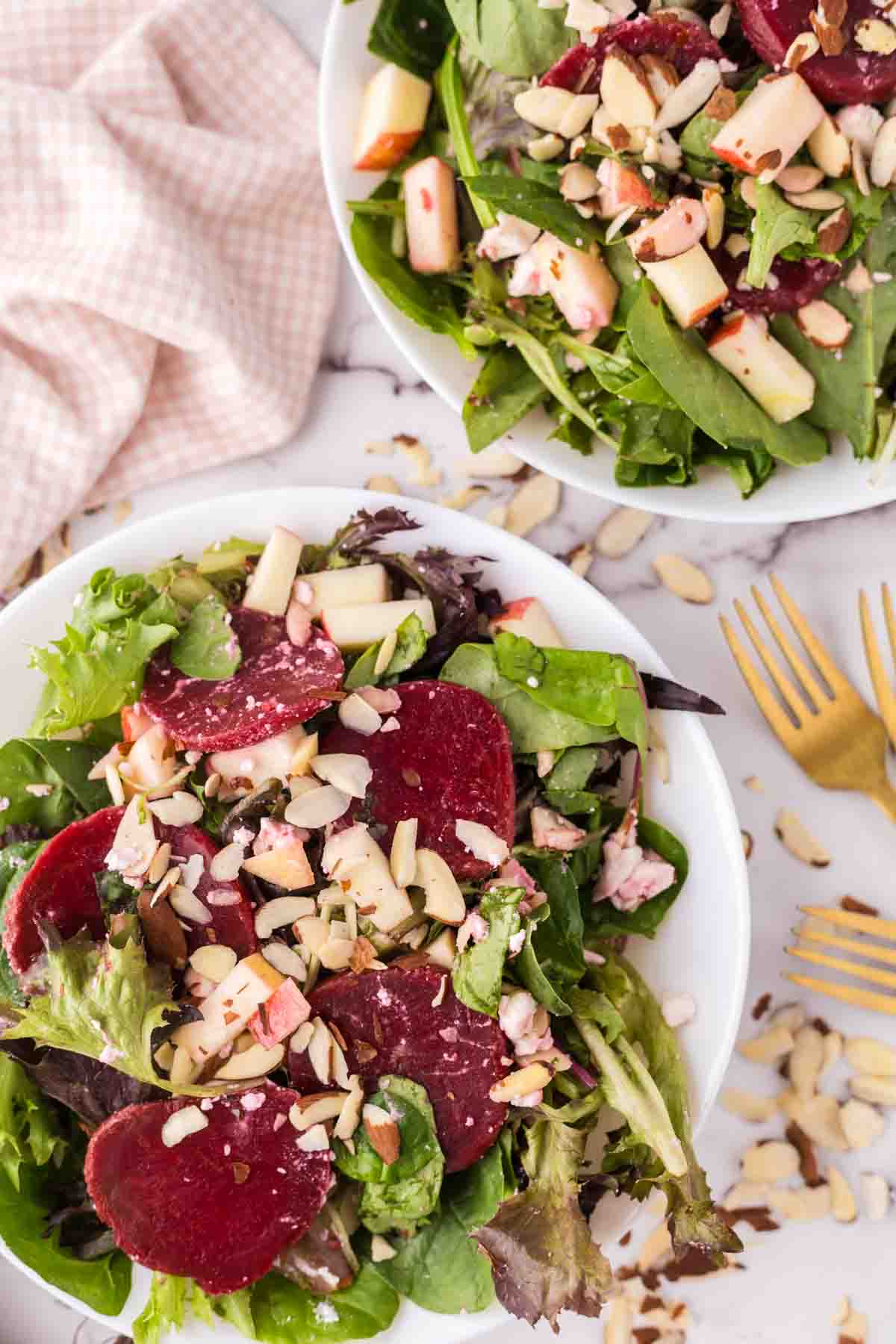 Two white bowls of beet salad with golden forks inside.