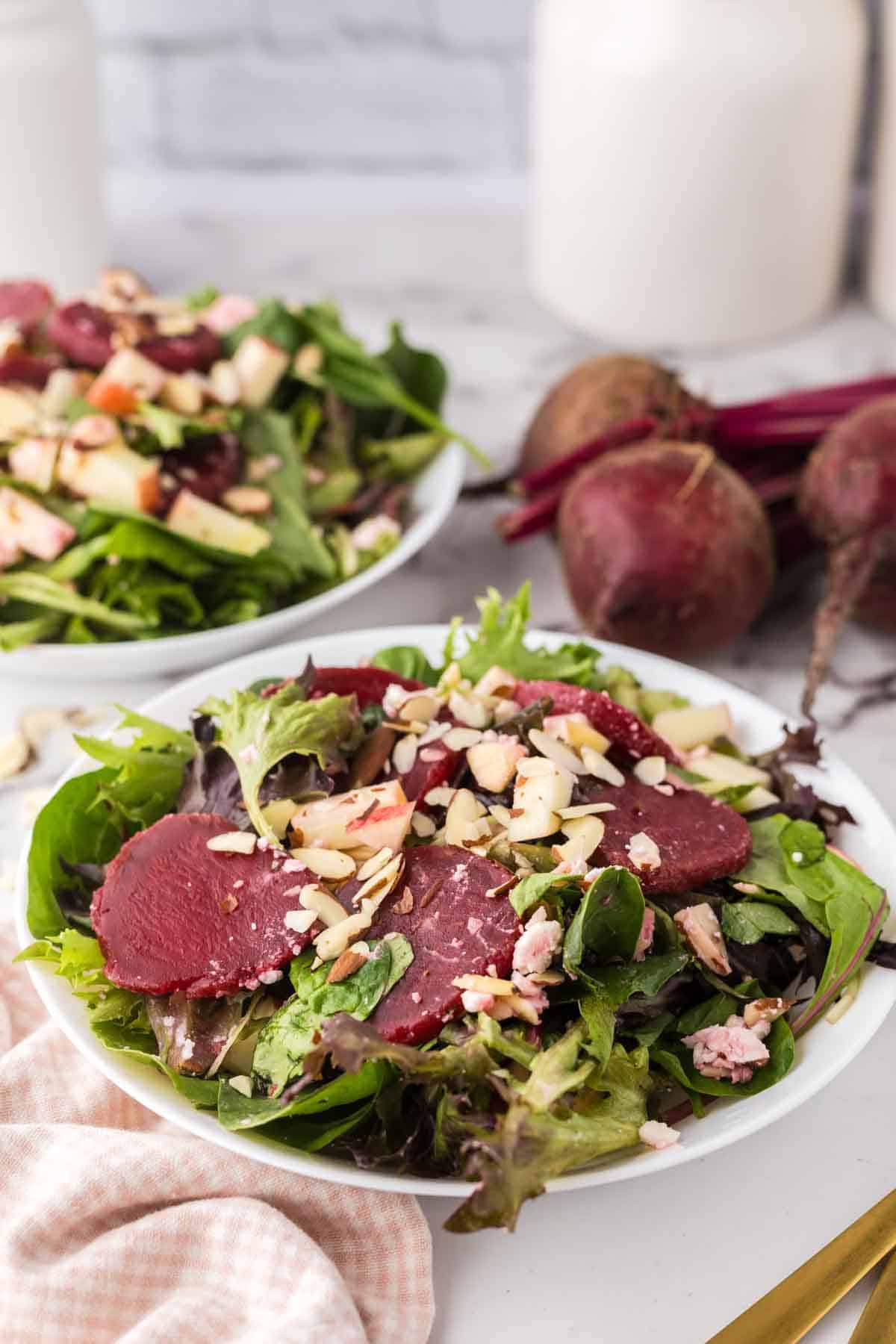 white bowls of beet salad with almonds and apples on top.