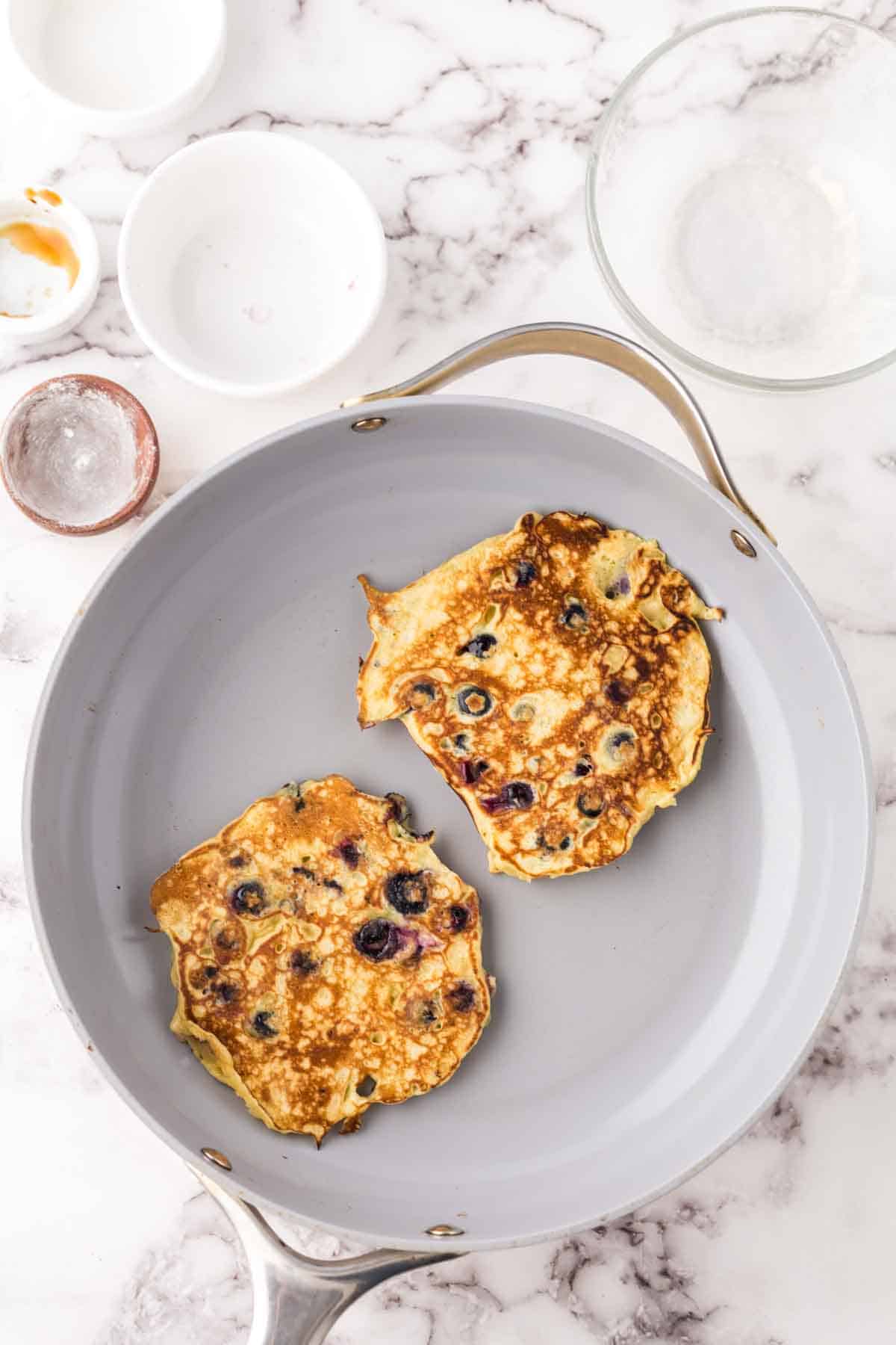pan with two cooked blueberry pancakes