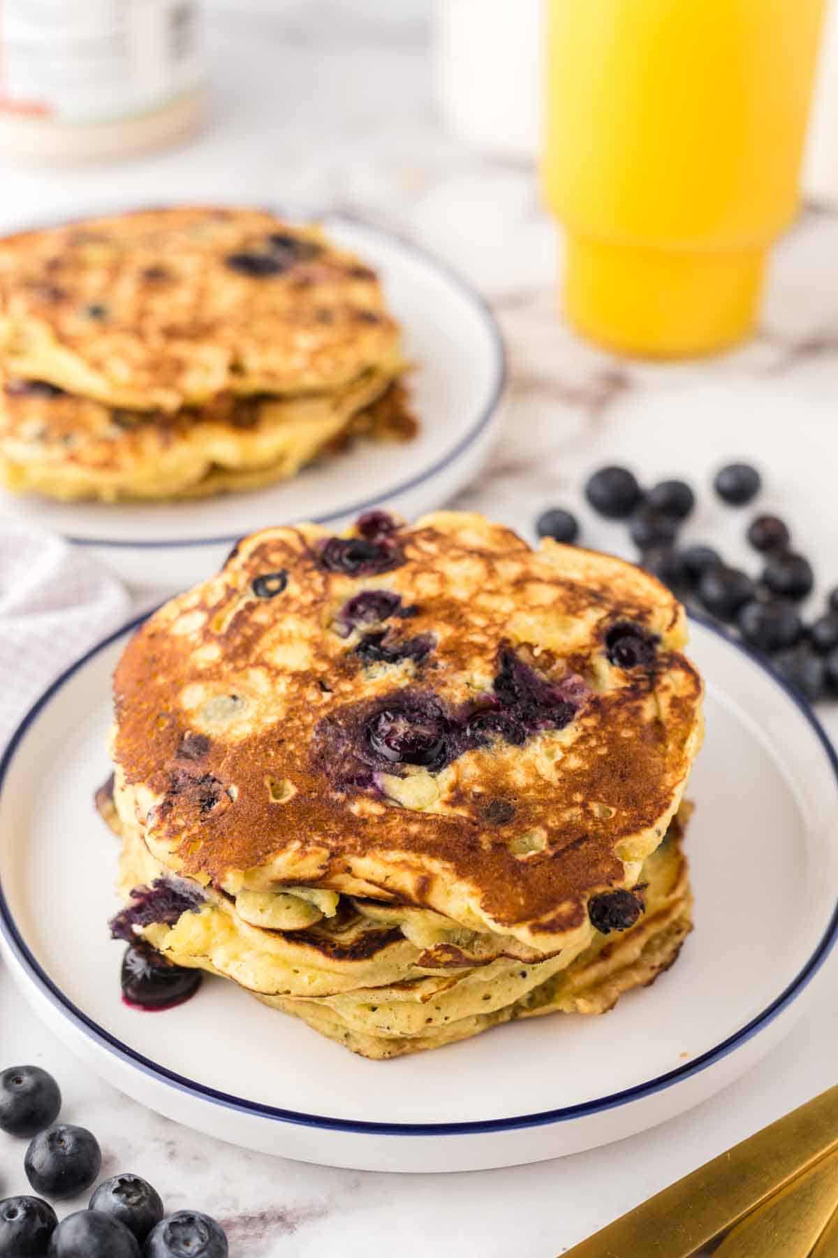 a round white plate with a blue outer edge with a stack of fluffy blueberry pancakes