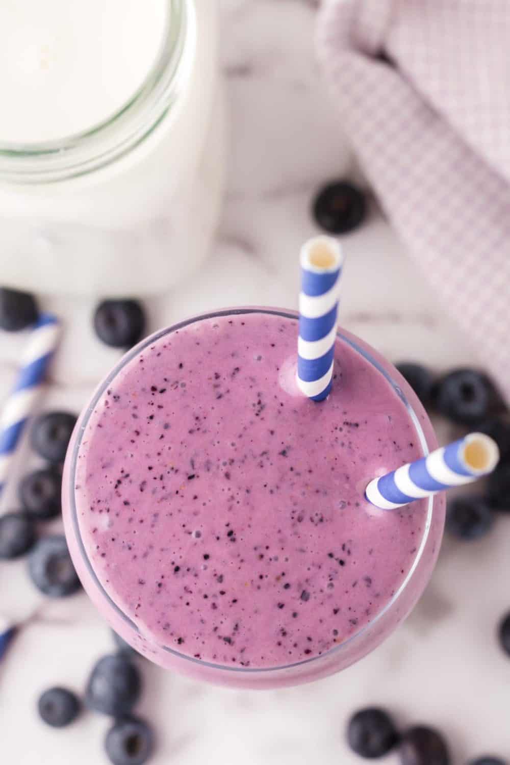 top view of a tall glass of blueberry smoothie with blue striped paper straws in the top