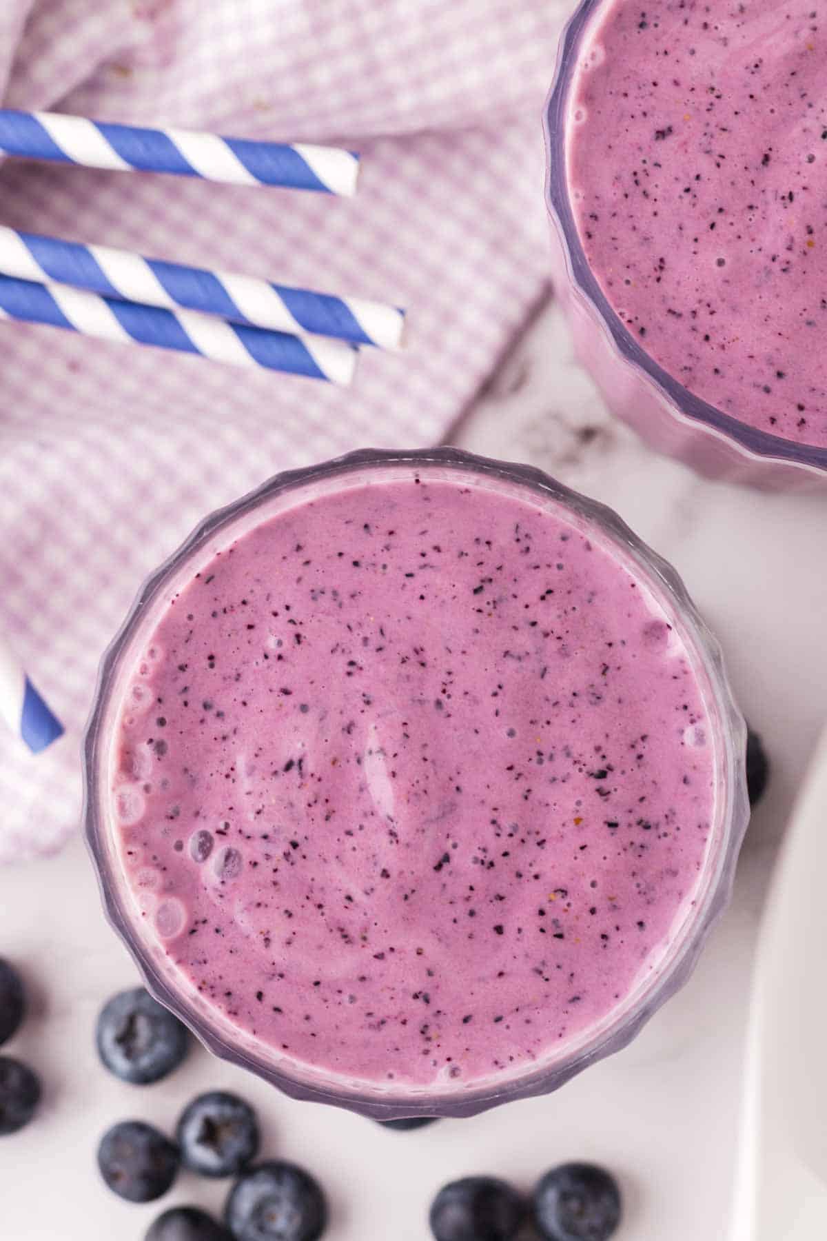 top view of blueberry smoothies in nice ribbed glasses with blue striped paper straws