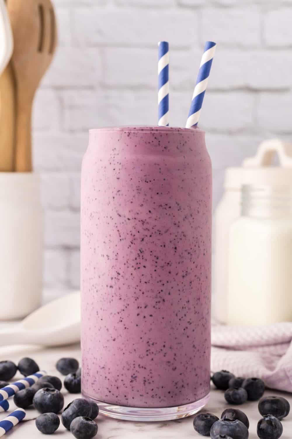 tall glass of blueberry smoothie with a blue striped paper straw