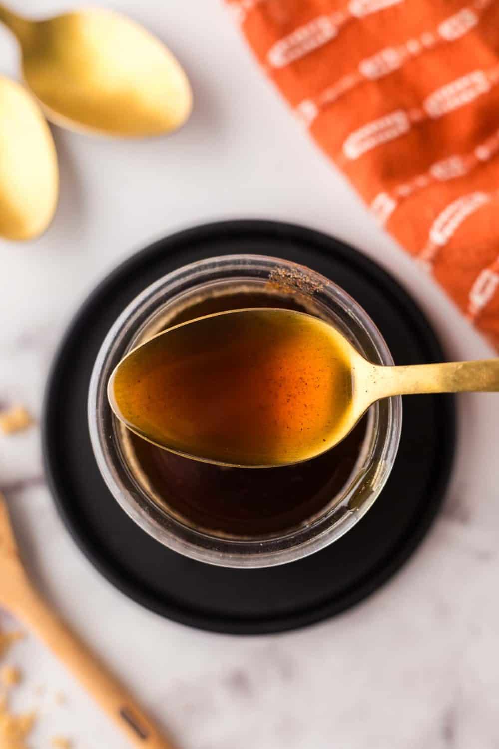 Golden spoon of brown sugar syrup over a small glass jar.