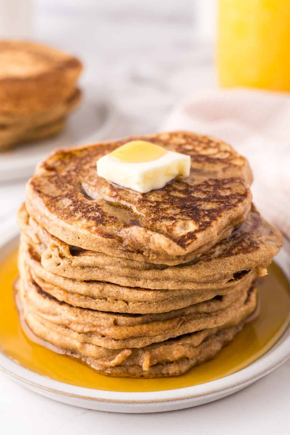 a stack of buckwheat pancakes on a round plate with a pad of butter and syrup on top