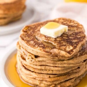 a stack of buckwheat pancakes on a round plate with a pad of butter and syrup on top