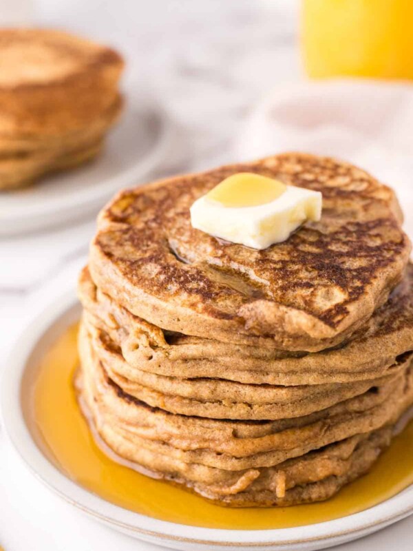 a stack of buckwheat pancakes on a round plate with a pad of butter and syrup on top