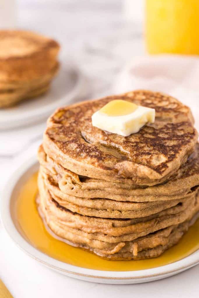 a stack of buckwheat pancakes on a round plate with a pad of butter and syrup on top