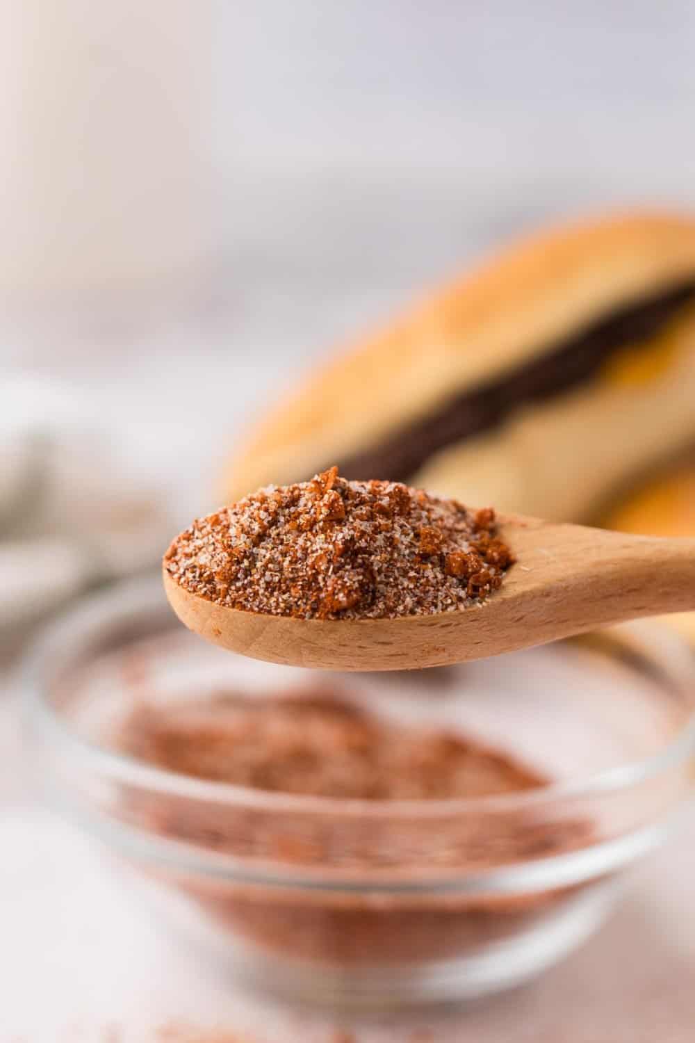 side view of a wooden spoonful of burger seasoning over a clear mixing bowl