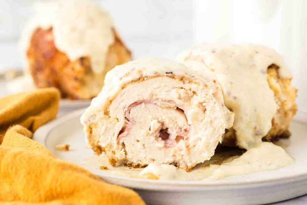 end view sliced chicken cordon bleu roll browned to a golden crunchy smothered in sauce on a plate