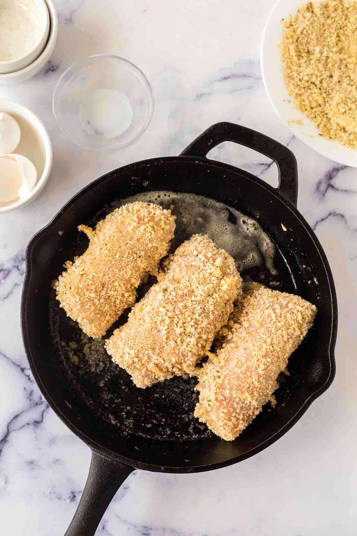 breaded chicken cordon bleu being browned and lightly fried in a cast iron pan