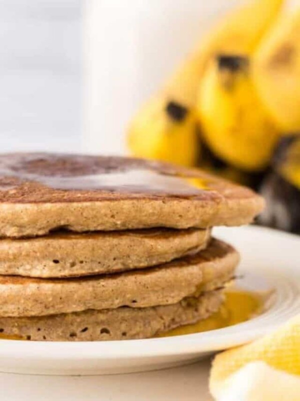 a stack of banana oatmeal pancakes on a white plate with syrup on top.