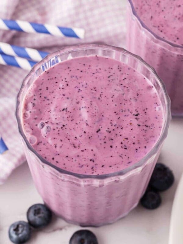 blueberry smoothies in nice ribbed glasses with blue striped paper straws.