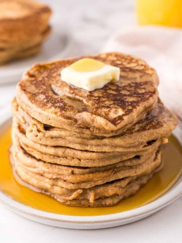 a stack of buckwheat pancakes on a round plate with a pad of butter and syrup on top.