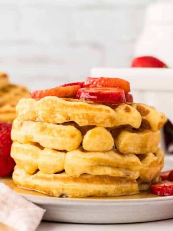 a stack of buttermilk waffles with syrup and fresh strawberries.