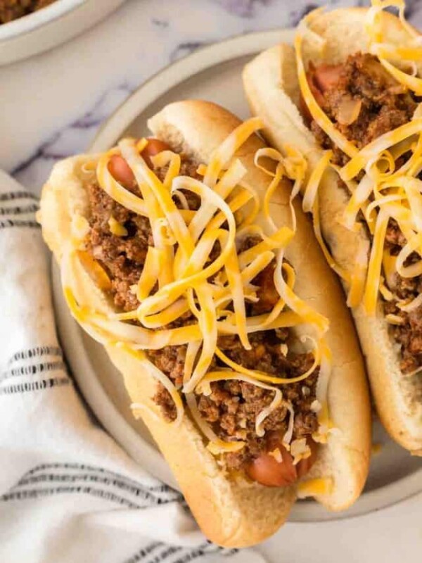round grey plate with chili dogs and shredded cheese on top.