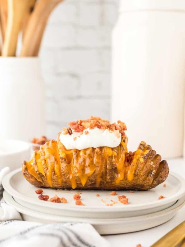 sliced hasselback potatoes with melted cheese on a round plate add sour cream and bacon bits