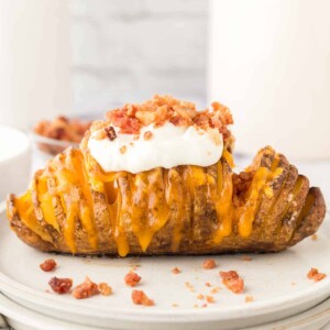 sliced hasselback potatoes with melted cheese on a round plate add sour cream and bacon bits