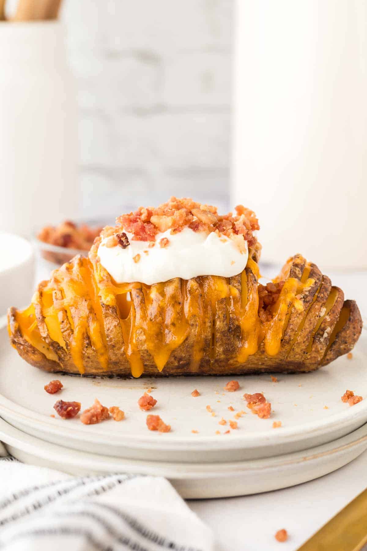 sliced hasselback potatoes with melted cheese on a round plate add sour cream and bacon bits