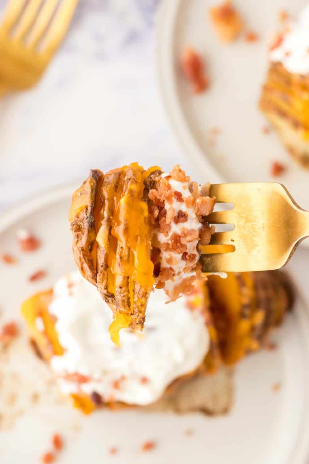 POV forkful of hasselback potatoes with melted cheese with sour cream and bacon bits