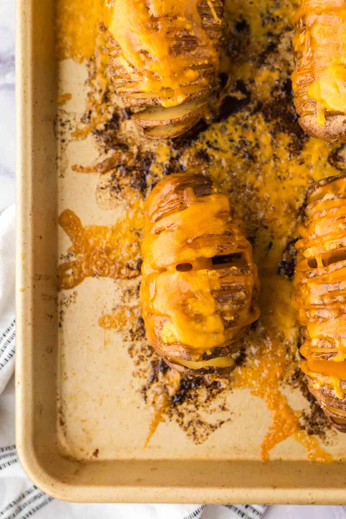 sliced hasselback potatoes with melted cheese on a baking sheet