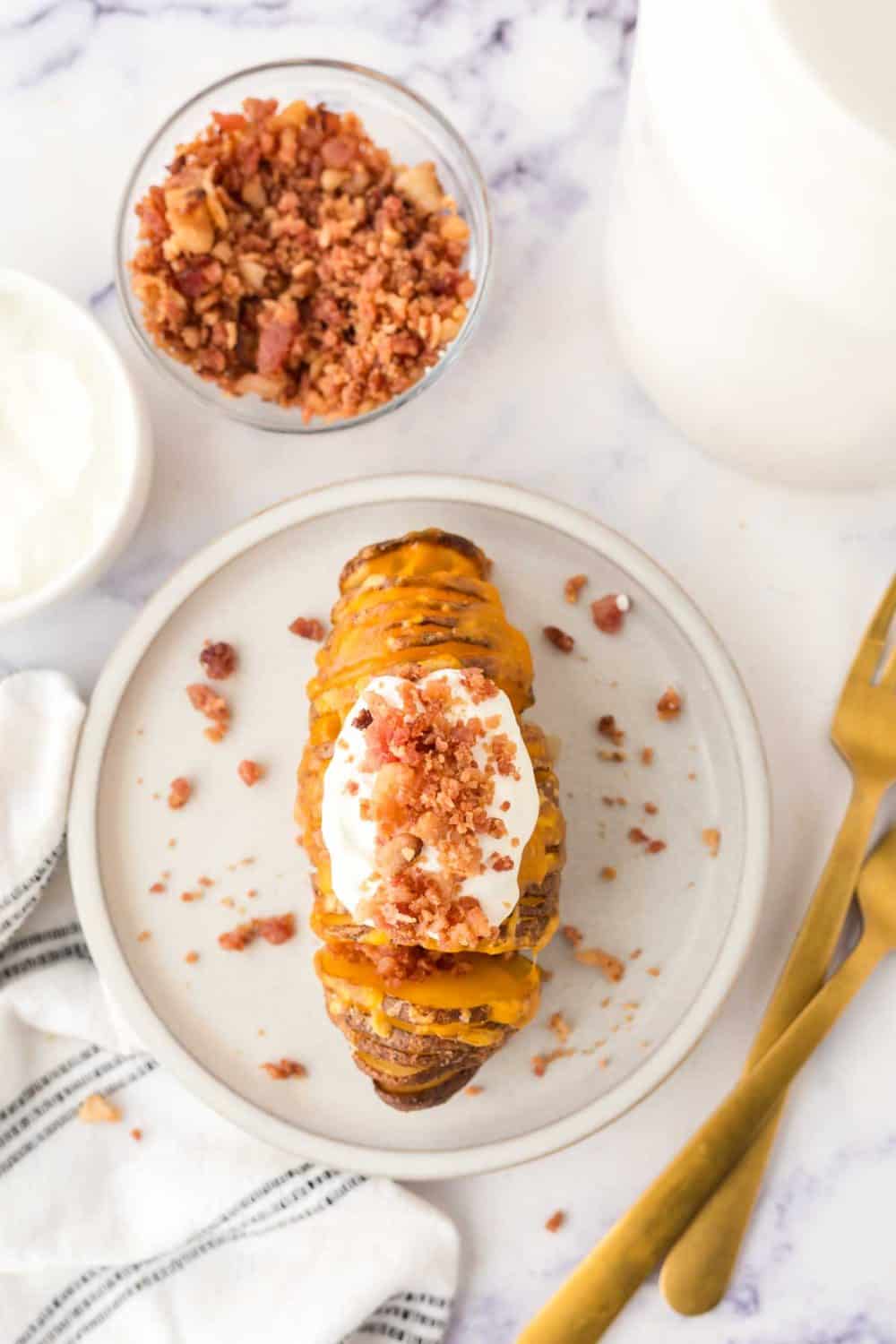 sliced hasselback potatoes with melted cheese on a round plate add sour cream and bacon bits