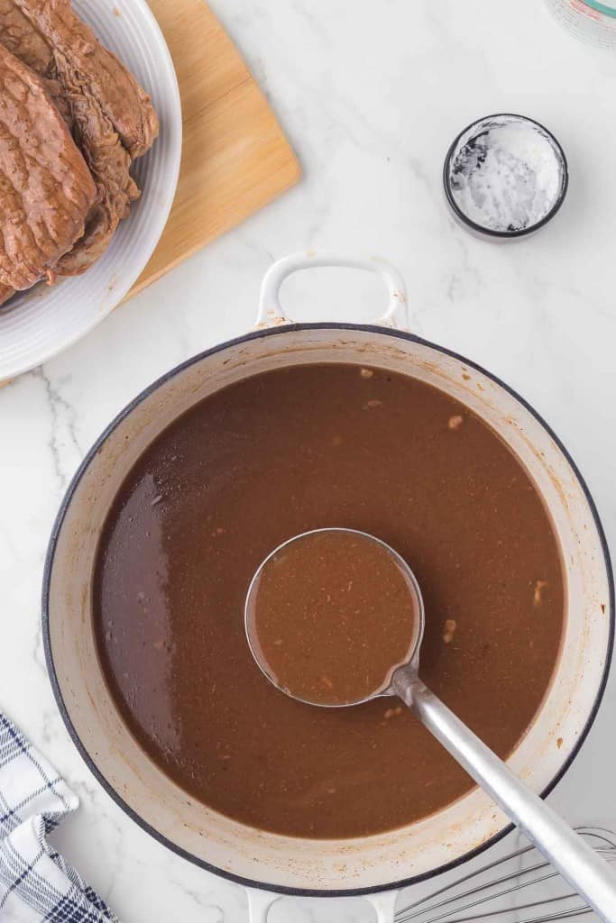 white dutch pot with liquid to make gravy and a ladle inside.