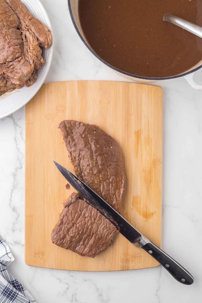 cooked round beef steak with gravy to the side.