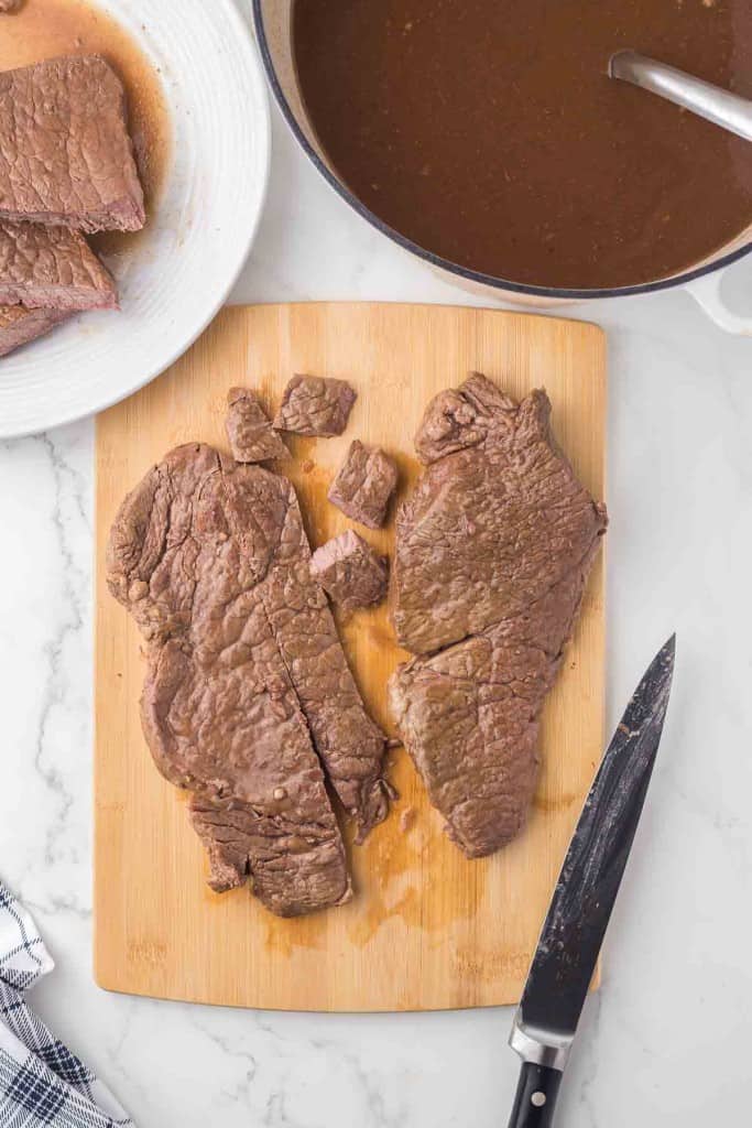 cooked round beef steak with gravy to the side.