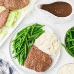 cooked round beef steak with green beens and mashed potatoes on a dinner plate with gravy to the side.