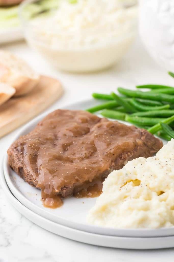 cooked round beef steak with green beens and mashed potatoes on a dinner plate.
