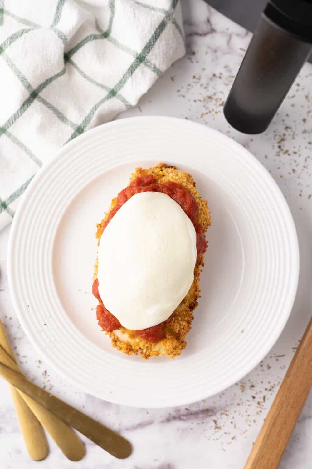 crispy air fried chicken parmesan with red sauce and melted mozzarella on a white plate.