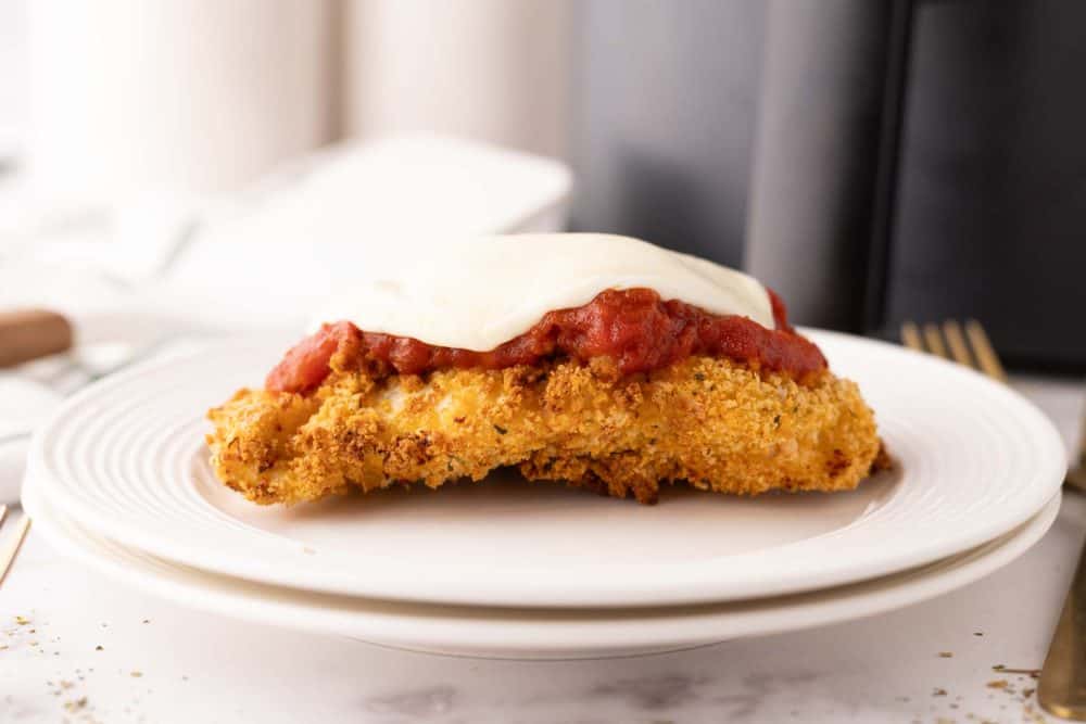 crispy air fried chicken parmesan with red sauce and melted mozzarella on a white plate.