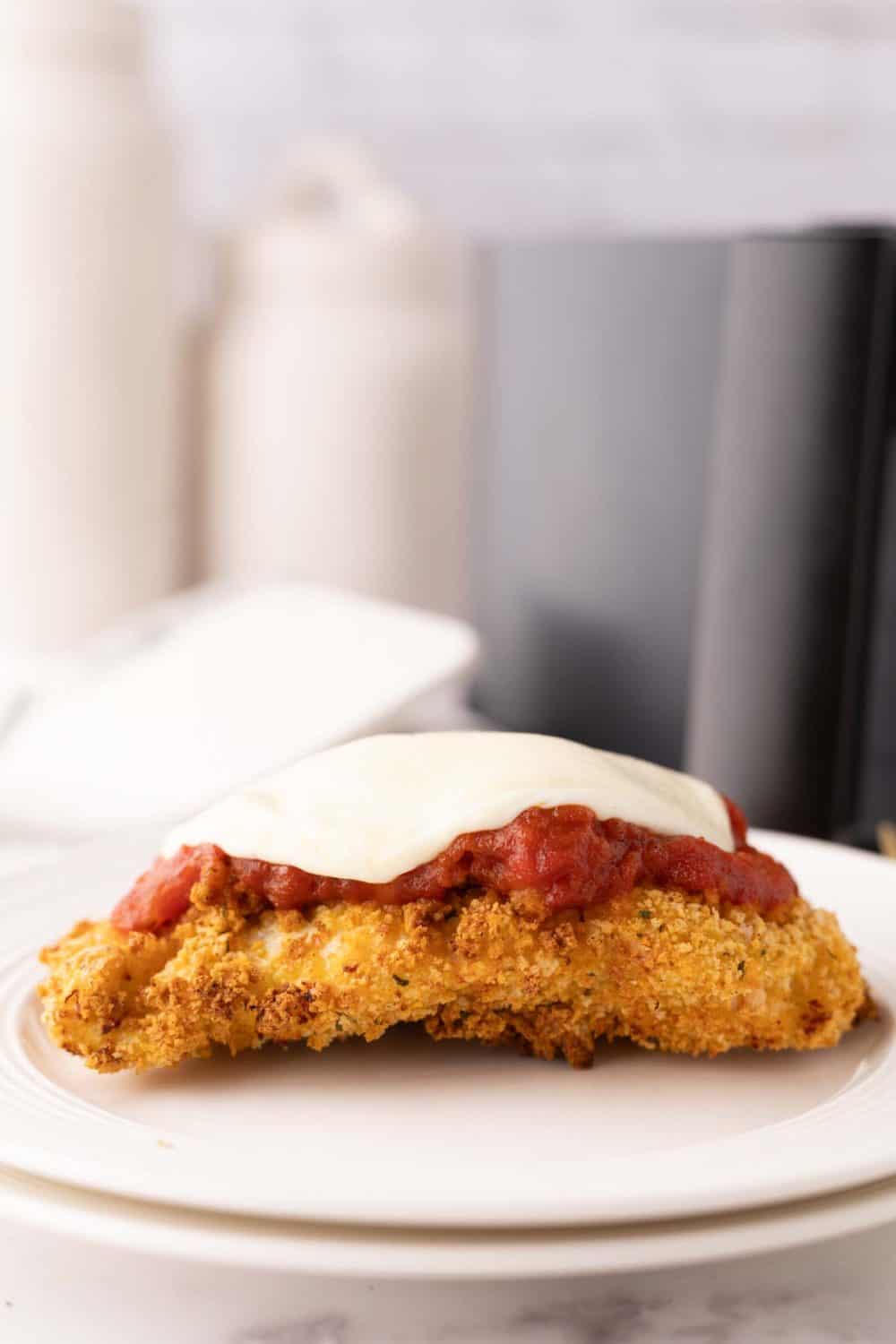 crispy air fried chicken parmesan with red sauce and melted mozzarella on a white plate.