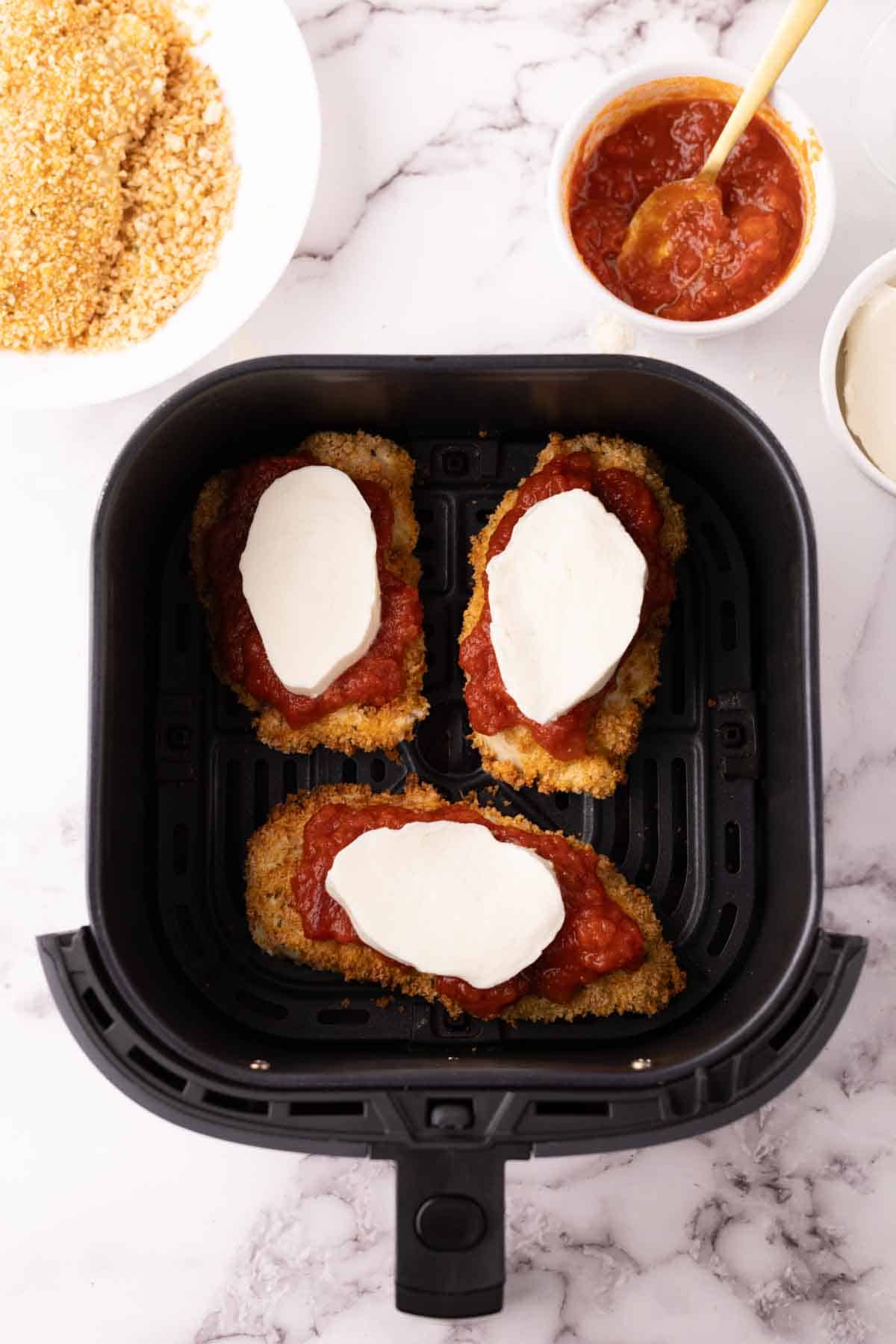 crispy air fried chicken parmesan with red sauce and melted mozzarella in an air fryer basket.