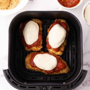 crispy air fried chicken parmesan with red sauce and melted mozzarella in an air fryer basket.