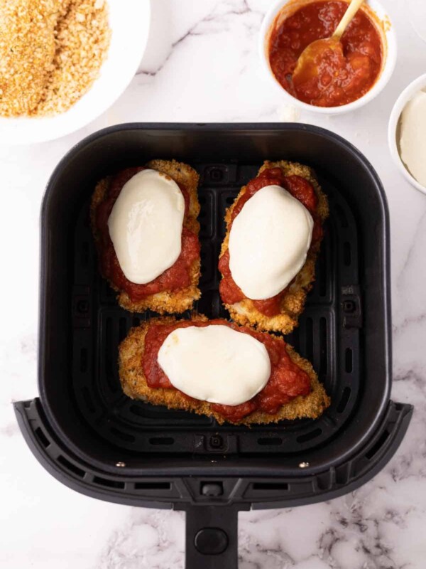 crispy air fried chicken parmesan with red sauce and melted mozzarella in an air fryer basket.