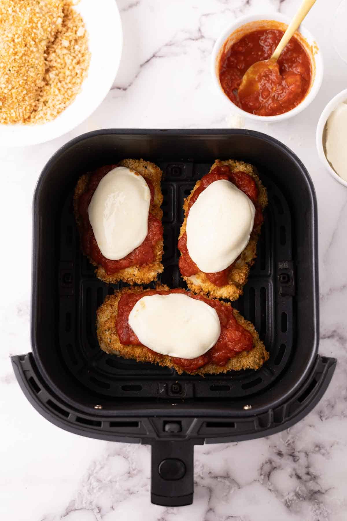 crispy air fried chicken parmesan with red sauce and melted mozzarella in an air fryer basket.