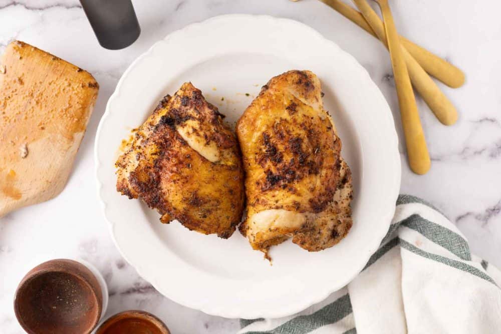 air fried crispy skinned chicken thighs on a white plate with gold forks to the side.
