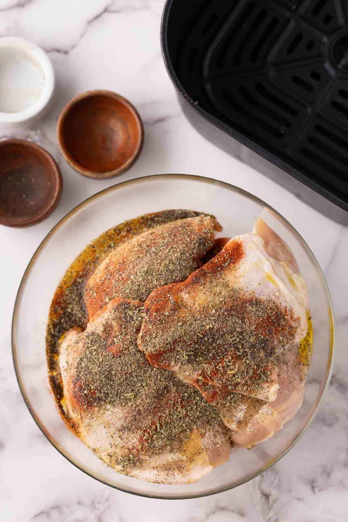 raw chicken thighs seasoned and marinating in a clear bowl.