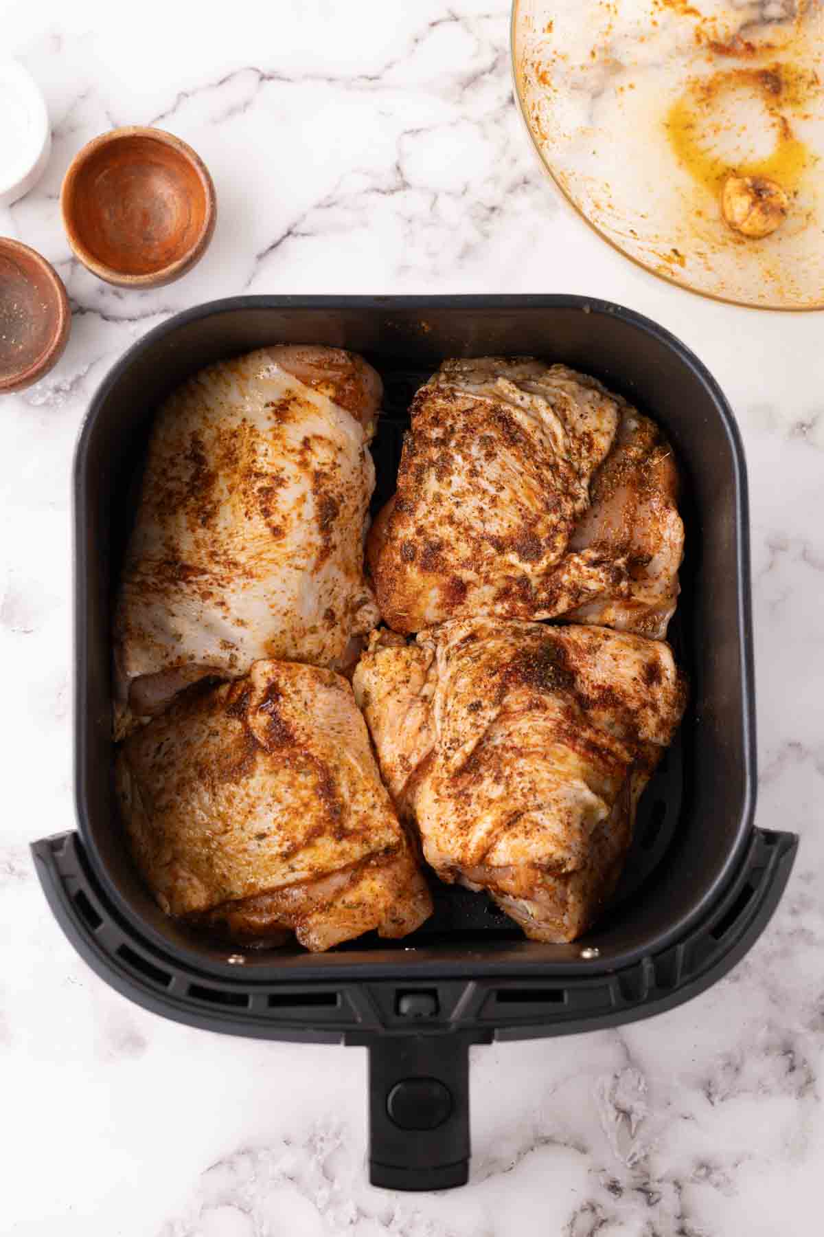 uncooked chicken thighs in a black air fryer basket.