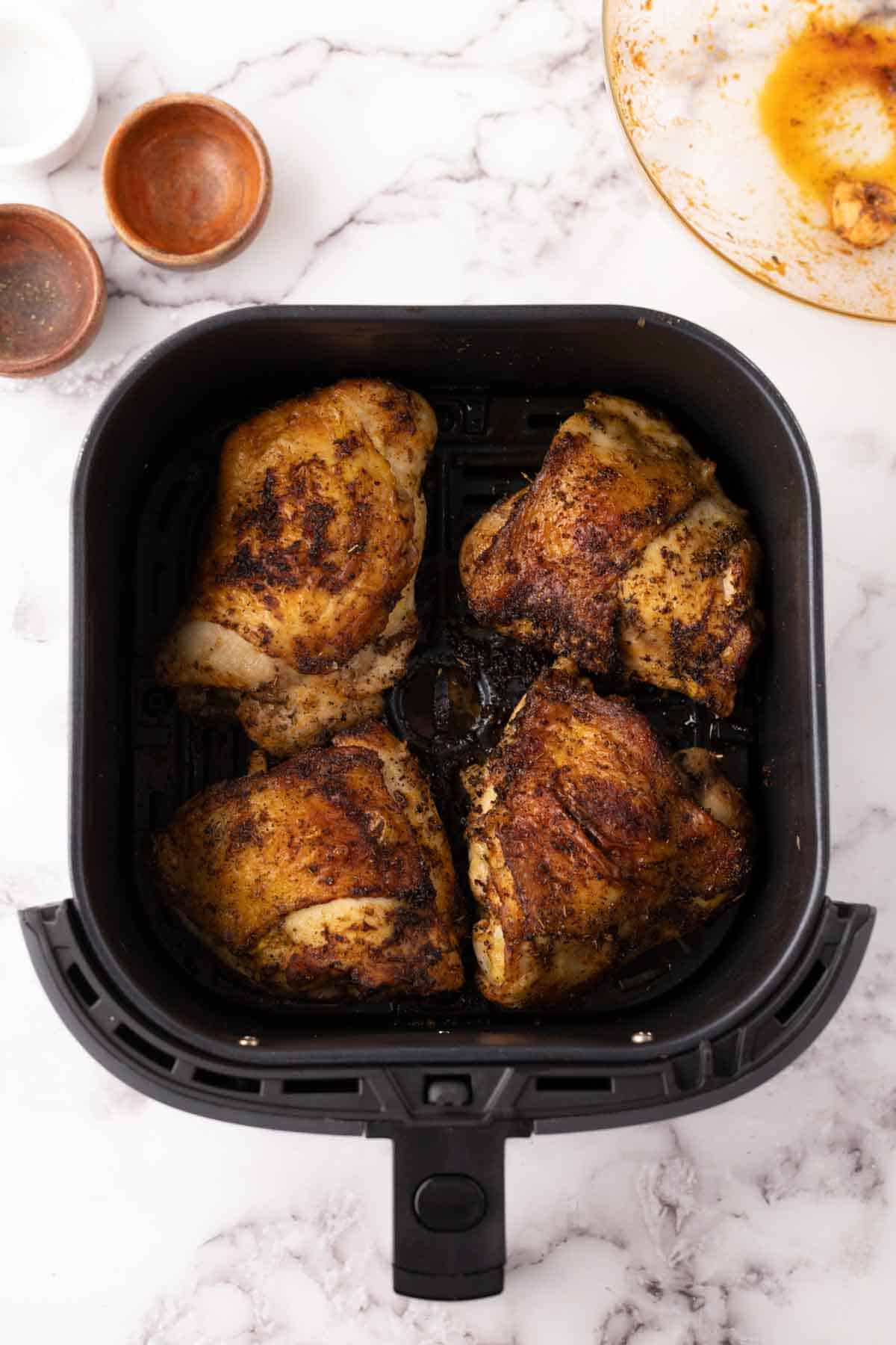 air fried crispy skinned chicken thighs in a black air fryer basket.
