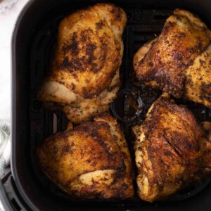 air fried crispy skinned chicken thighs in a black air fryer basket.