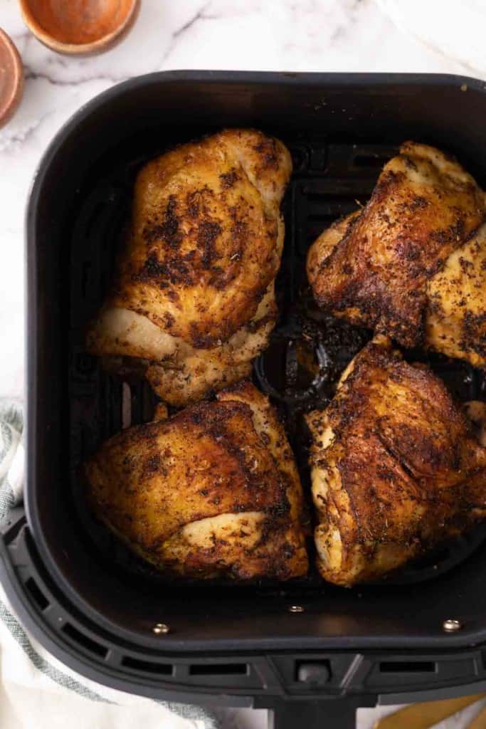 air fried crispy skinned chicken thighs in a black air fryer basket.