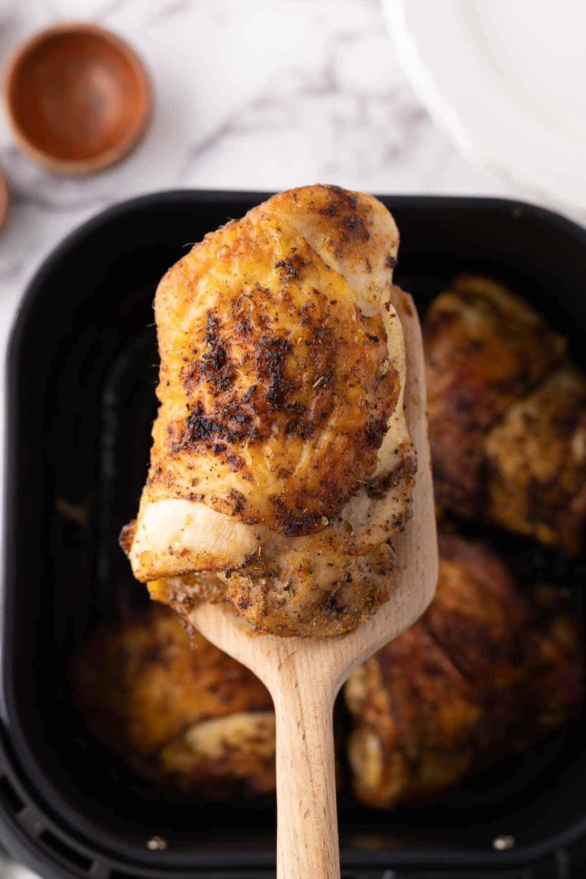 air fried crispy skinned chicken thighs a wooden spatula held over the air fryer.