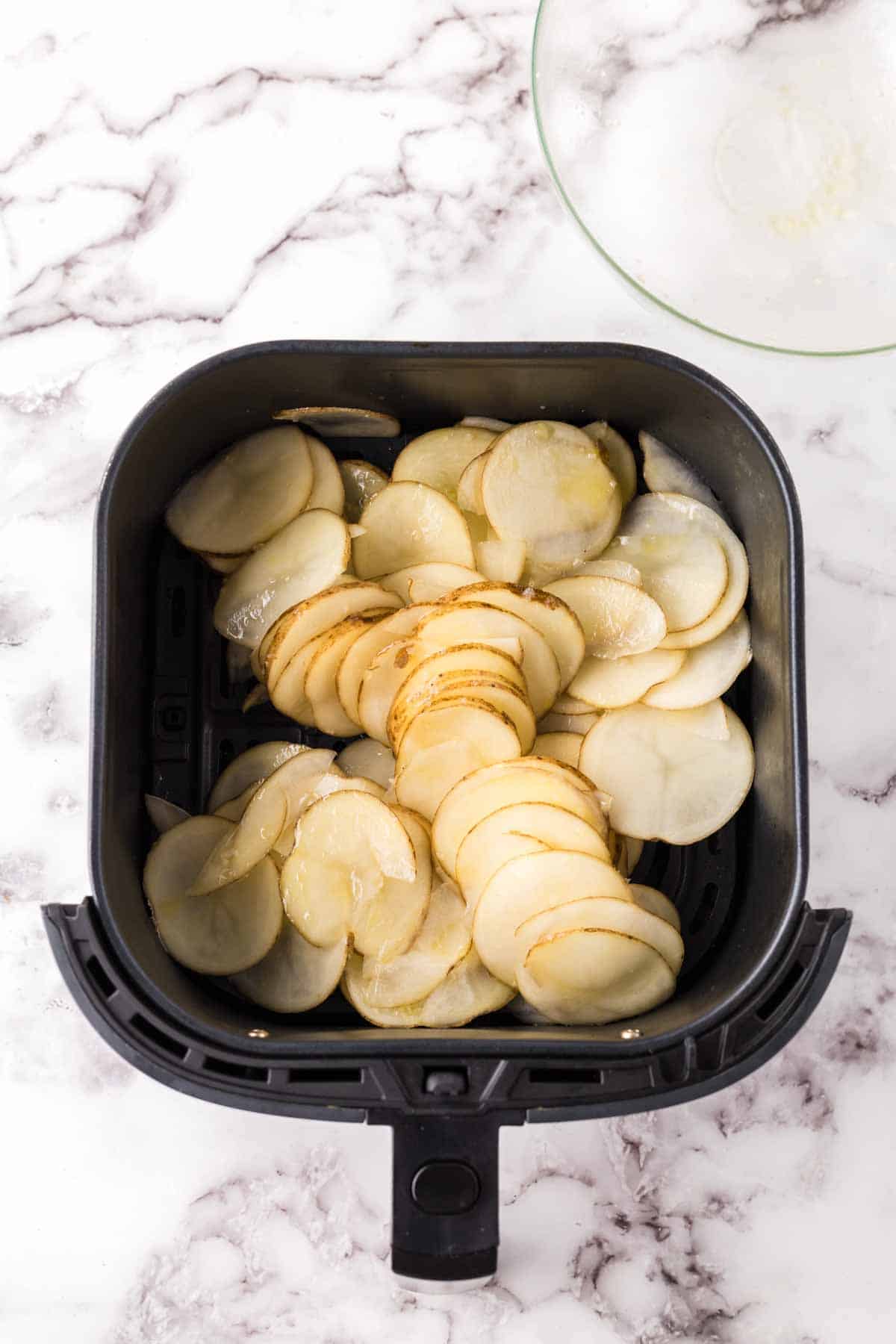black air fryer with raw sliced potatoes.