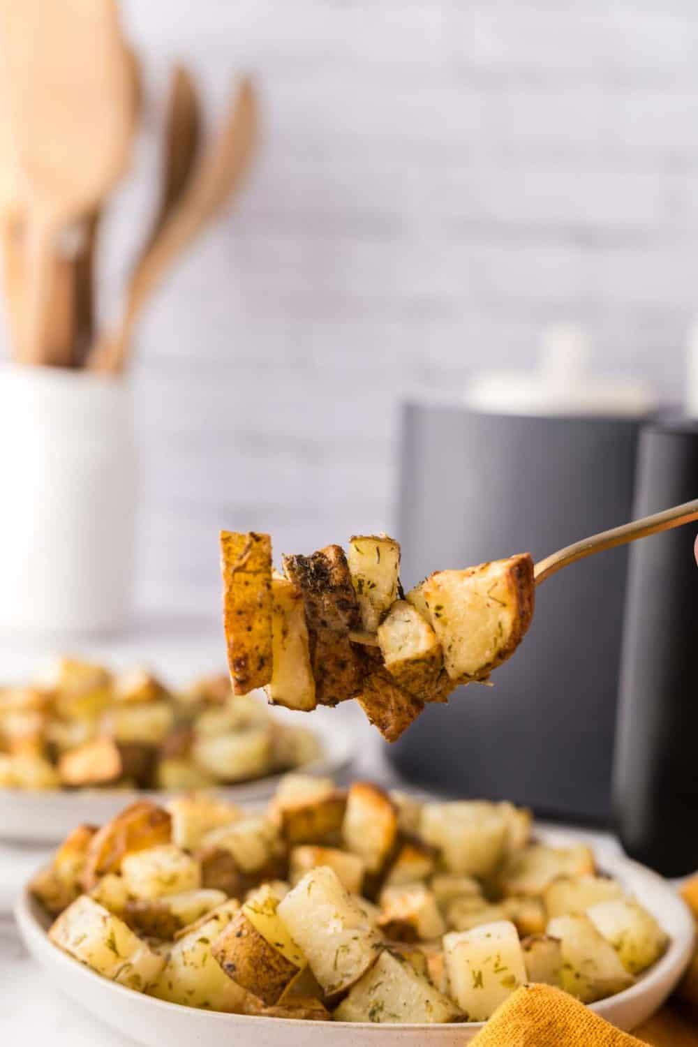 air fried roasted potatoes on a gold fork over a white plate of other potatoes.