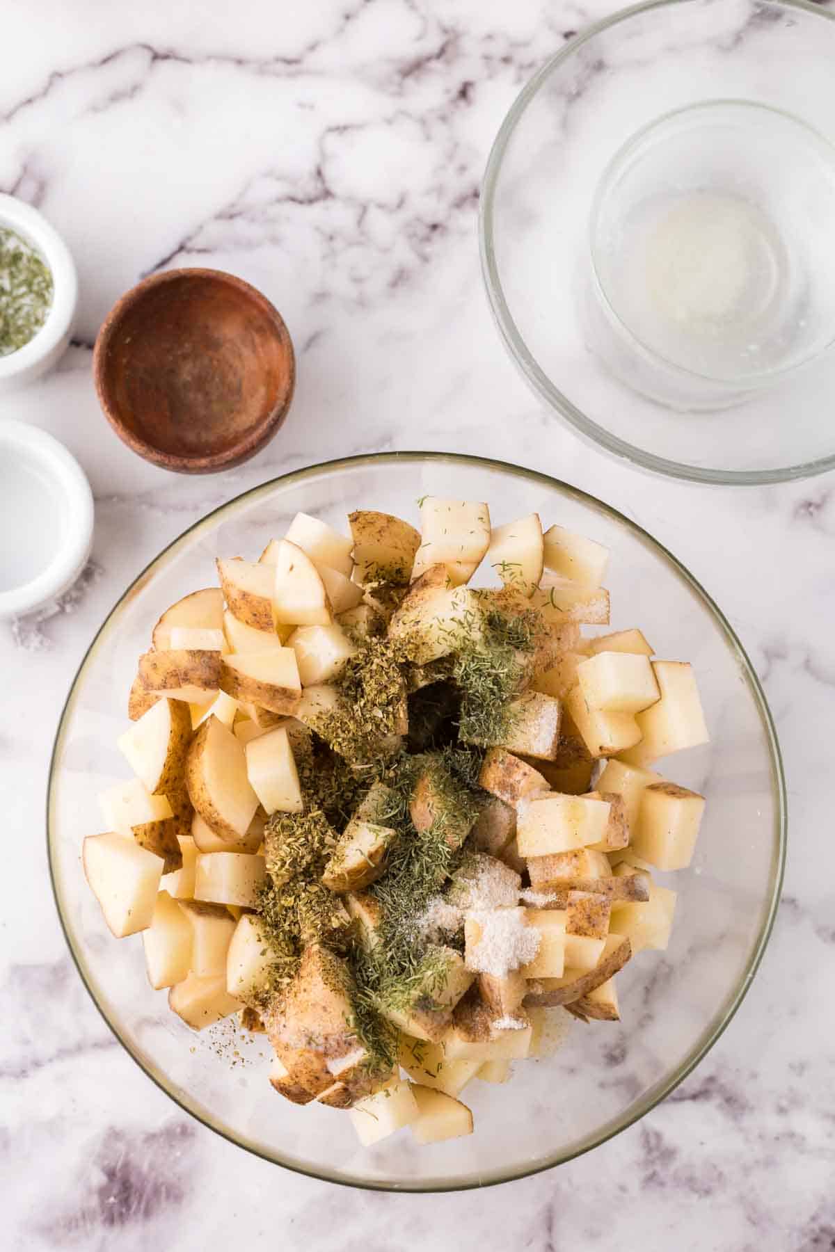 glass mixing bowl with raw and seasoned potatoes.