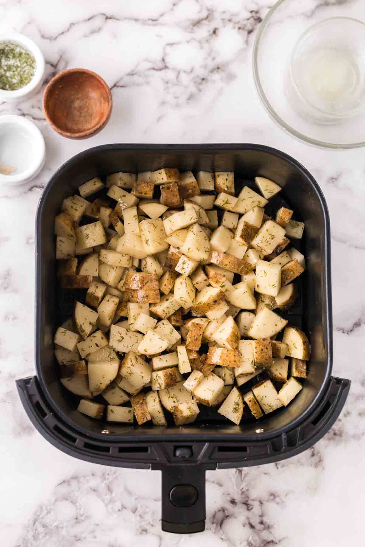 black air fryer basket with diced uncooked potatoes.
