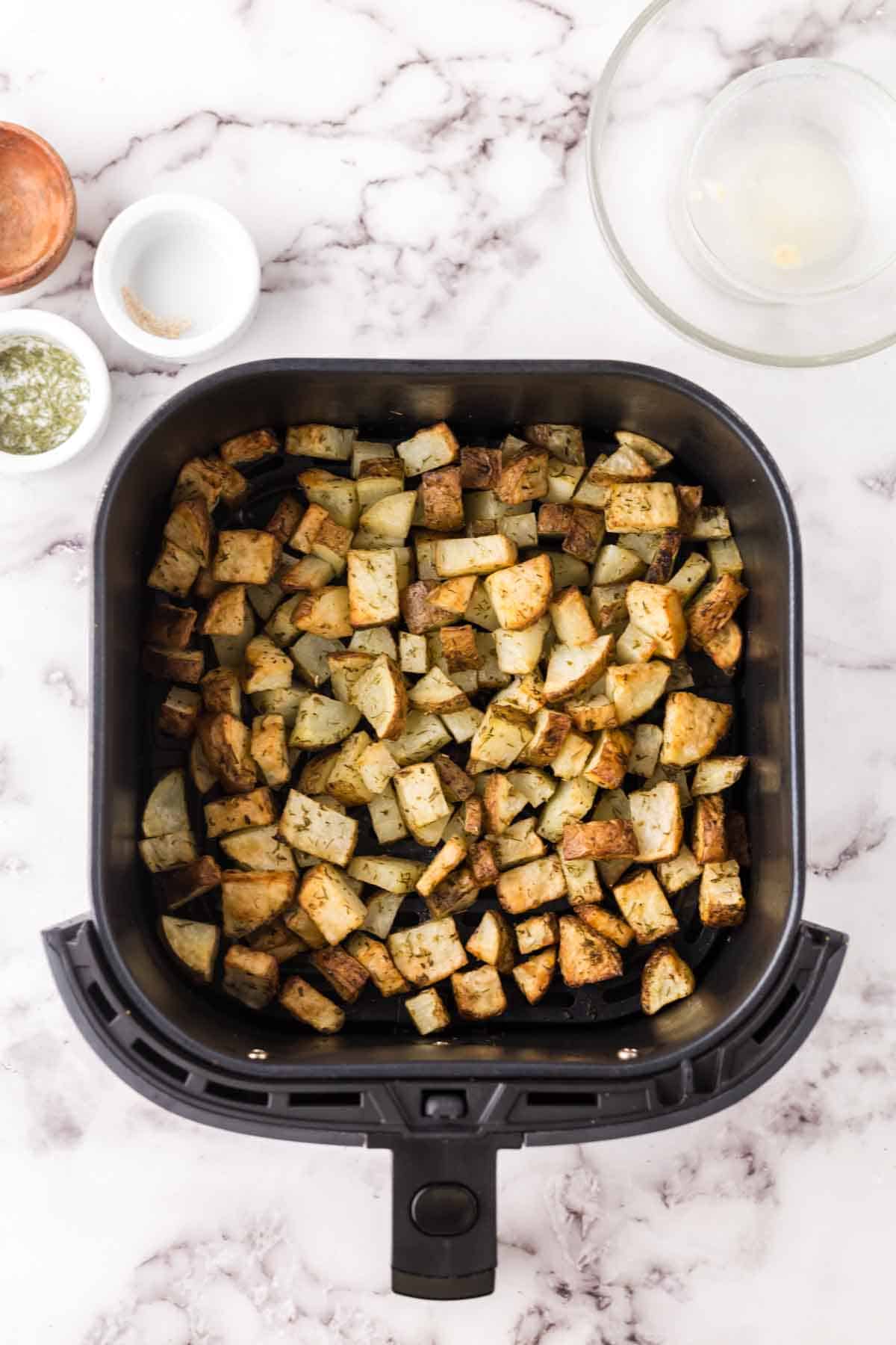 black air fryer basket with diced cooked potatoes.